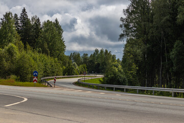 Winding rural road surrounded by dense trees and greenery, featuring a 70 km/h speed limit sign...
