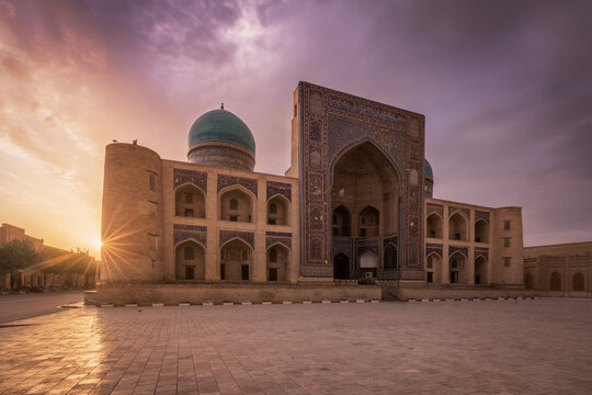 View of the sun bursting on a historic mosque, and intricate tile work under a sunset sky, Bukhara, Bukhara Region, Uzbekistan.