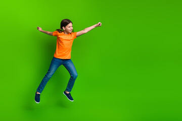 Excited young girl jumping enthusiastically in casual clothes with a vibrant green background...