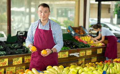 Male seller working in supermarket and lays out fresh oranges on counter