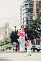 Fototapeta premium Stylish young woman with luggage in urban cityscape, enjoying a sunny day outdoors in a casual chic outfit