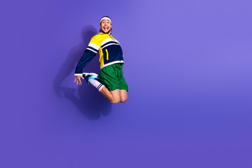 Energetic male athlete in vibrant retro sportswear performing a mid-air leap against a solid violet...