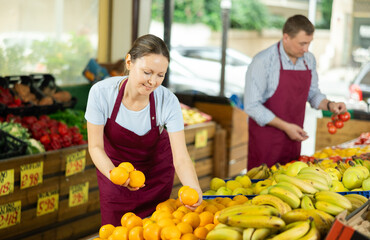 Positive saleswoman in apron offering oranges on the supermarket