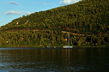 A peaceful autumn scene featuring sailboats gently anchored on a calm lake, with a forest-covered...