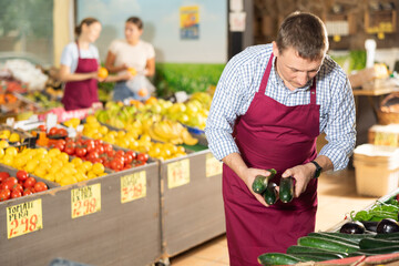 Man seller working in supermarket and lays out fresh cucumber on counter