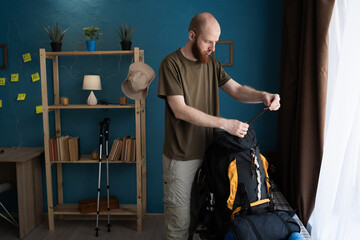 bearded hiker packing backpack for mountain trip