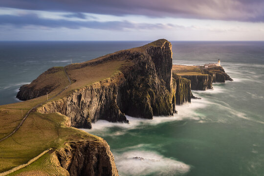 View of neist point cliff, kissed by the soft glow of twilight, with a distant lighthouse standing sentinel, Isle of Skye, Scotland, United Kingdom.