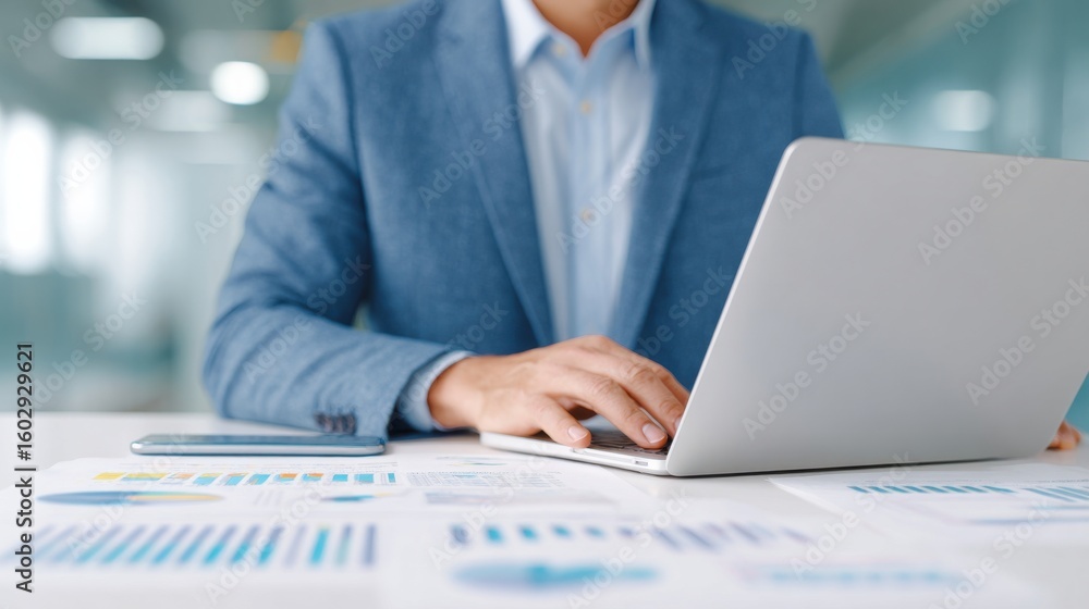 Poster a man in a suit is typing on a laptop in front of a table with a lot of graphs