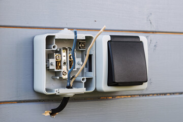Outdoor socket installation in progress on light wooden wall shows exposed wires and open cover, illustrating electrical safety and setup.