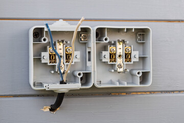Double outdoor socket installation on gray wooden wall shows open casing and exposed wires, clearly demonstrating step-by-step connection process.