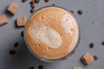Autumn latte in clear glass with airy foam surrounded by coffee beans and sugar cubes creates cheerful, inviting vibe for seasonal enjoyment.