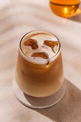 Chilled autumn latte in a stylish glass with ice cubes and creamy froth glows in warm sunlight, evoking cozy seasonal vibes.
