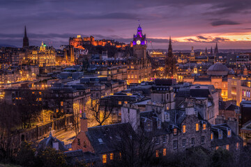 View of Edinburgh Castle perched atop a volcanic crag, illuminated against the twilight sky, casting a warm glow over the historic city, Edinburgh, Scotland, United Kingdom.