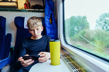 Teen boy using smartphone while riding train alone