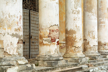 Weathered stone columns with peeling paint and exposed brick reveal the faded grandeur of an abandoned historic building entrance.