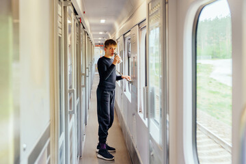 Teen boy drinking from cup in train corridor