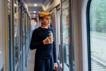 Teen boy holding bottle and watching train window reflection