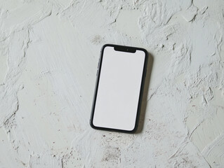 A silver smartphone with a blank white screen lies on a textured surface under soft lighting.