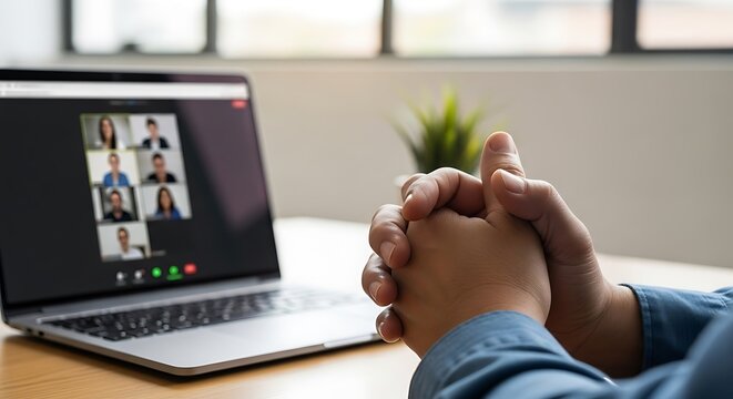 A person participates in a video conference call on a laptop with multiple participants visible on the screen