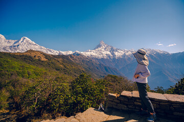 The front view of a woman standing on a cement yard with the Machapuchare peak is covered by snow on top in the background, Mardi Himal trek, Nepal. Idea for a nature background with copy space.
