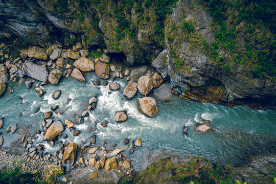 High-angle view of forest and river flowing through Taroko National Park, Taiwan. Clear blue water streams over rocks with moss in the crevices of the mountain. Idea for a nature background.