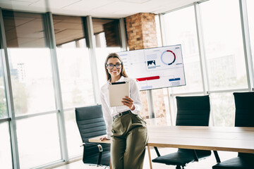 Charming young businesswoman in modern office with report and charts displaying, embracing professional success