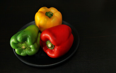 A plate of red, green and yellow capsicums on a black plate and black background. 