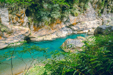 High-angle view of forest and river flowing through Taroko National Park, Taiwan. Clear blue water streams over rocks with moss in the crevices of the mountain. Idea for a nature background.