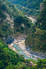High-angle view of forest and river flowing through Taroko National Park, Taiwan. Clear blue water streams over rocks with moss in the crevices of the mountain. Idea for a nature background.
