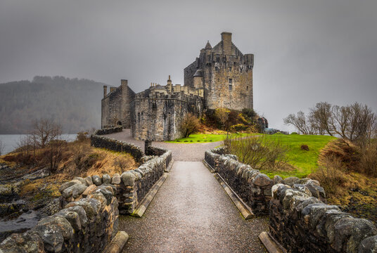 View of elean donan castle perched dramatically on a small island, connected by a rugged stone bridge under a moody sky, Dornie, Scotland, United Kingdom.