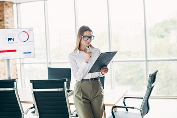 Busy businesswoman reviewing documents in a modern office workspace with a bright background and...