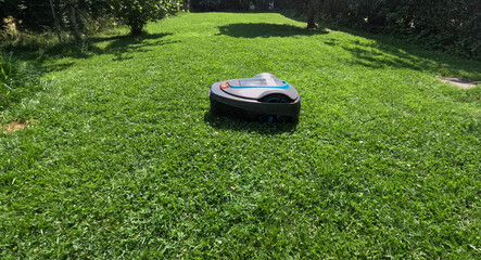 A robotic lawn mower cutting green lawn during a sunny day. The machine is scheduled to automatically cut daily and efficiently trims and maintains backyards