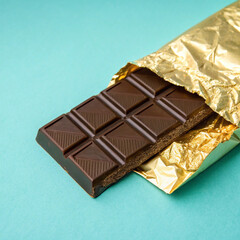 An elegant piece of dark chocolate resting on a golden wrapper against a colorful blue backdrop.