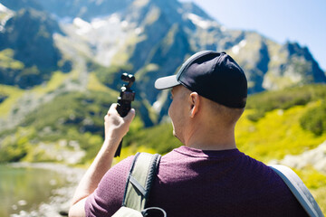 Beautiful panoramic view of a clear alpine lake surrounded by green forest and rugged mountain peaks under a bright blue sky. A peaceful summer day in nature, perfect for hiking, relaxation, and