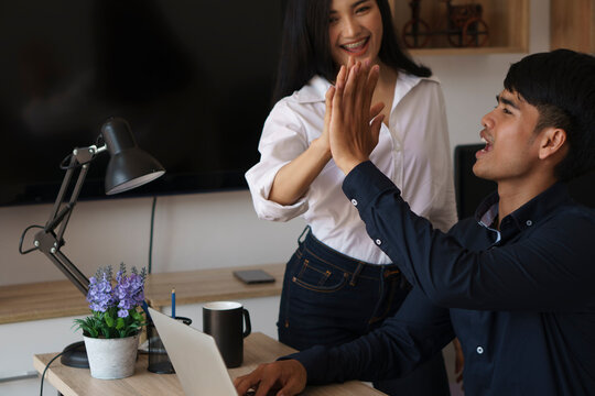 Happy Asian business team high-fiving in home office. Celebrating teamwork success in casual modern workspace.