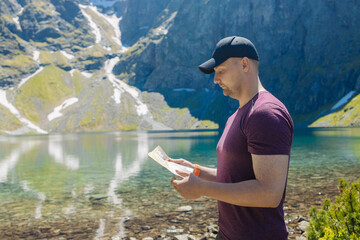 Male traveler standing near a scenic alpine lake with a map in hand Admiring the mountain view...