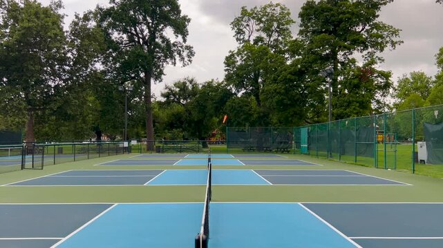 Outdoor Pickleball Courts. Side view of pickleball courts, looking across the nets of several courts in a row. Public city park setting with cloudy blue Summer sky.
