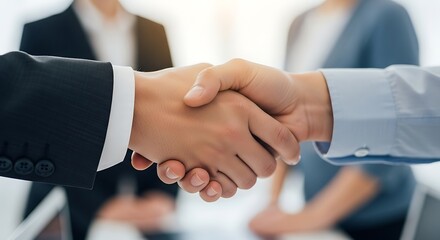 A handshake between two business partners with colleagues in the background