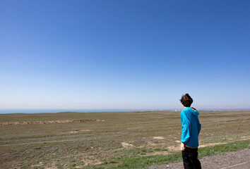 A person in a blue jacket looking at a vast open landscape under a clear blue sky
