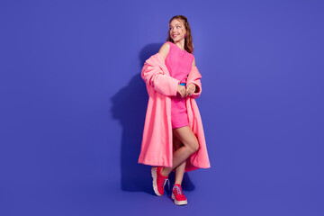 Elegant young woman in stylish pink outfit posing against a bold purple background, showcasing...