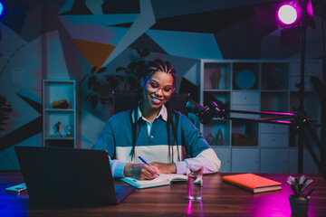 Charming female vlogger recording a podcast in a cozy home studio with neon lighting and...