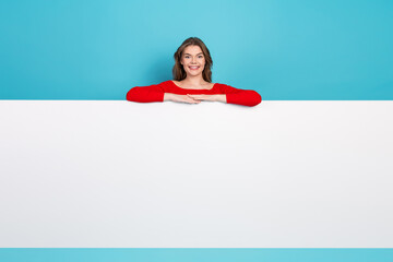 Joyful woman in a red top stands smiling against a turquoise background with a white board ready...