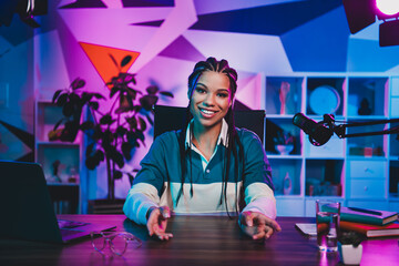 Enthusiastic young woman hosting a live podcast in a vibrant neon-lit home office environment,...