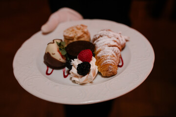 Delicious assortment of desserts served on a white plate at an elegant dining event during evening hours