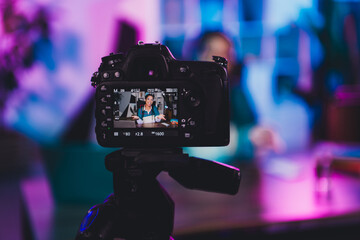 Professional female blogger recording content in neon-lit home office studio during evening with...