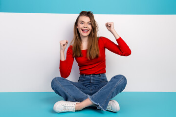 Young stylish woman in casual outfit celebrating success while seated on a vibrant background in an...