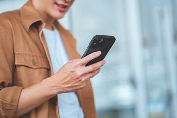 Close-up of asian man’s hands using smartphone while standing near shopping mall in city street...