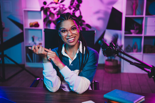 Charming woman blogger with microphone in neon-lit studio engaging in social media content creation and podcasting