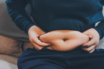 woman's hand holding excessive belly fat, overweight concept