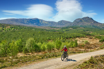 Fototapeta premium nice senior woman riding her electric mountain bike in the highlands of Glen Affric Nature reserve, Scotland, UK